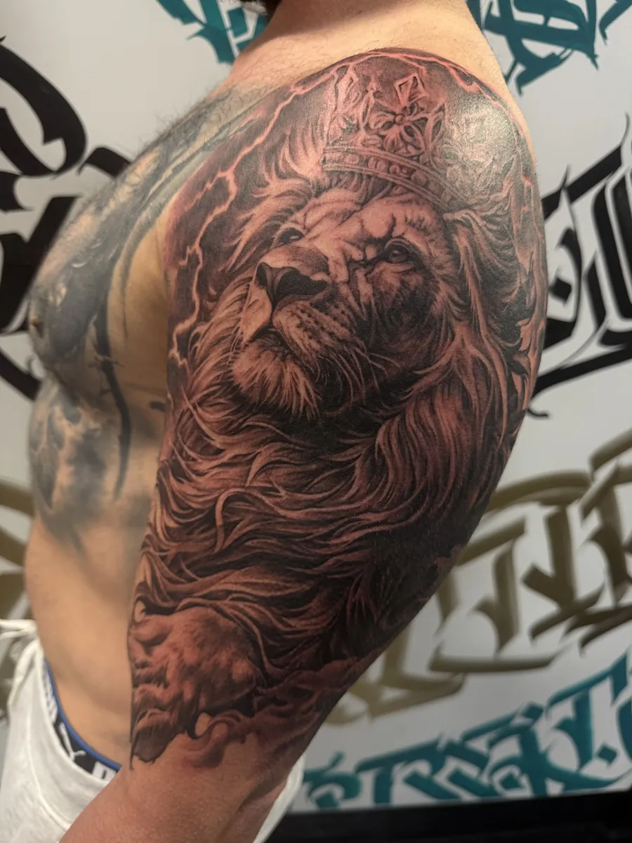 Black and grey lion with a crown and lightning shoulder tattoo by Moose, Calgary Tattoo Company