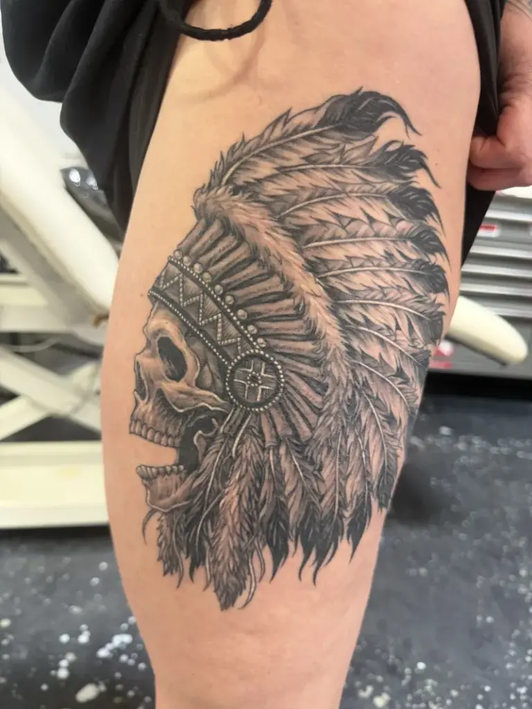 Black and grey skull in a feathered headdress tattoo by Moose, Calgary Tattoo Company